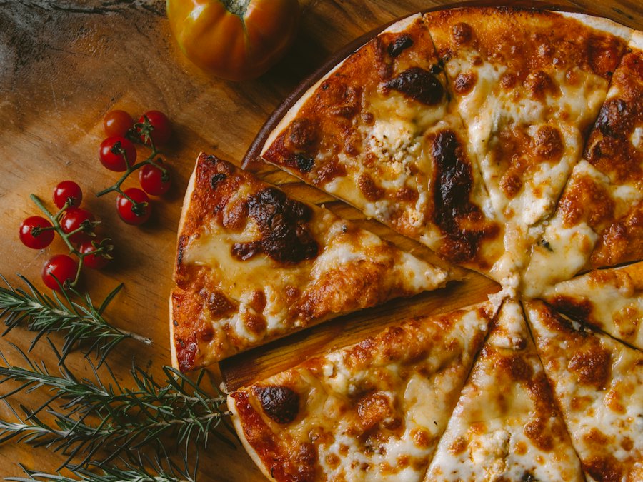 Sliced cheese pizza with cherry tomatoes and rosemary on a wooden board