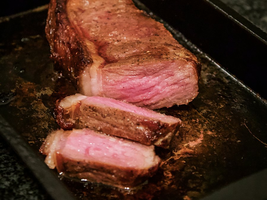 Sliced medium-rare grilled steak on a black tray