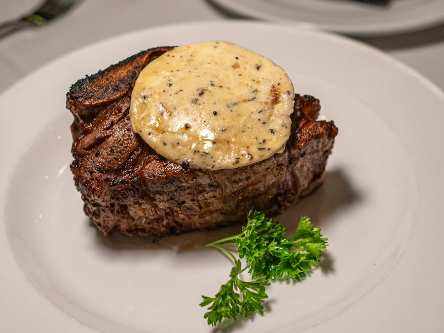 Bone-in filet mignon topped with butter sauce on a white plate